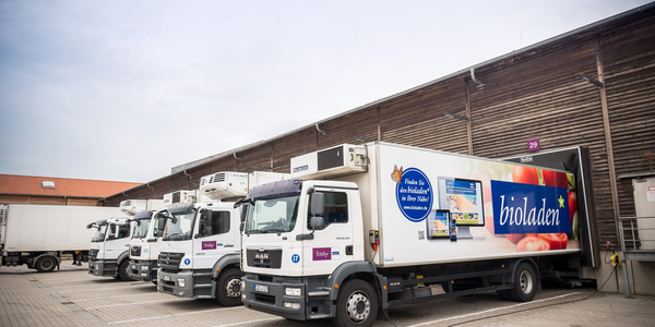 KI generiert: Eine Reihe von Lieferwagen vor einem Gebäude. Text: "bioladen".