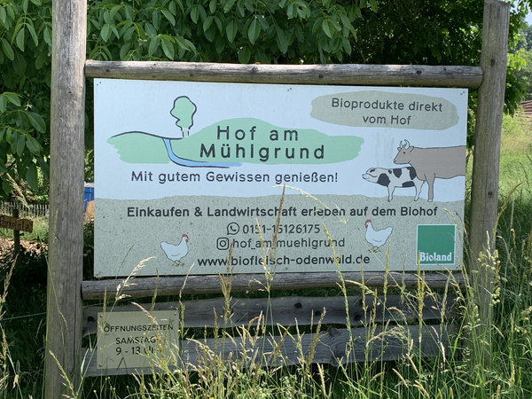 KI generiert: Schild eines Biohofs mit Kontaktinfos: "Hof am Mühlgrund, Bioprodukte direkt vom Hof. www.biofleisch-odenwald.de."