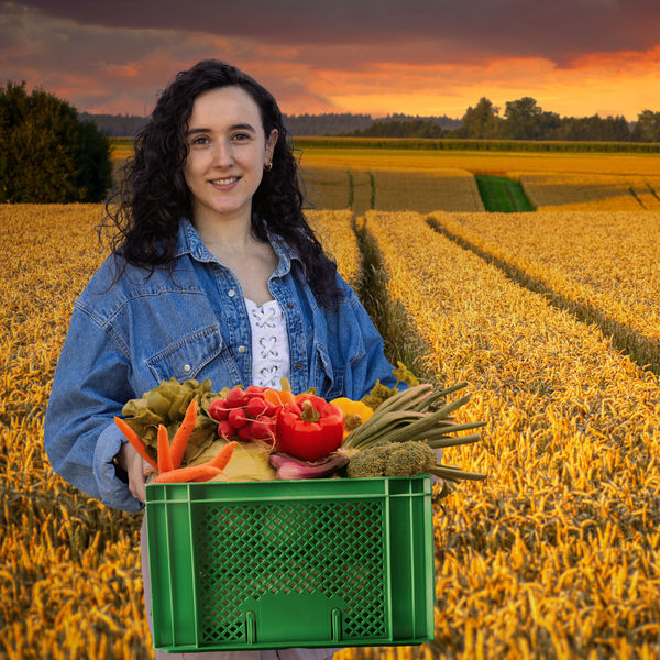 KI generiert: Frau hält Gemüsekiste in einem Getreidefeld bei Sonnenuntergang.
